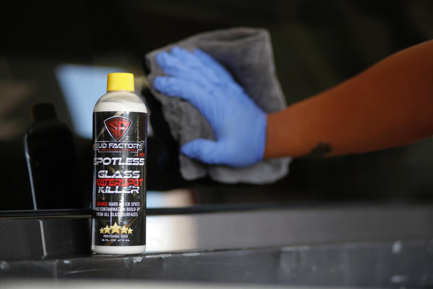 Gloved hand wiping glass next to a Spotless X2 bottle